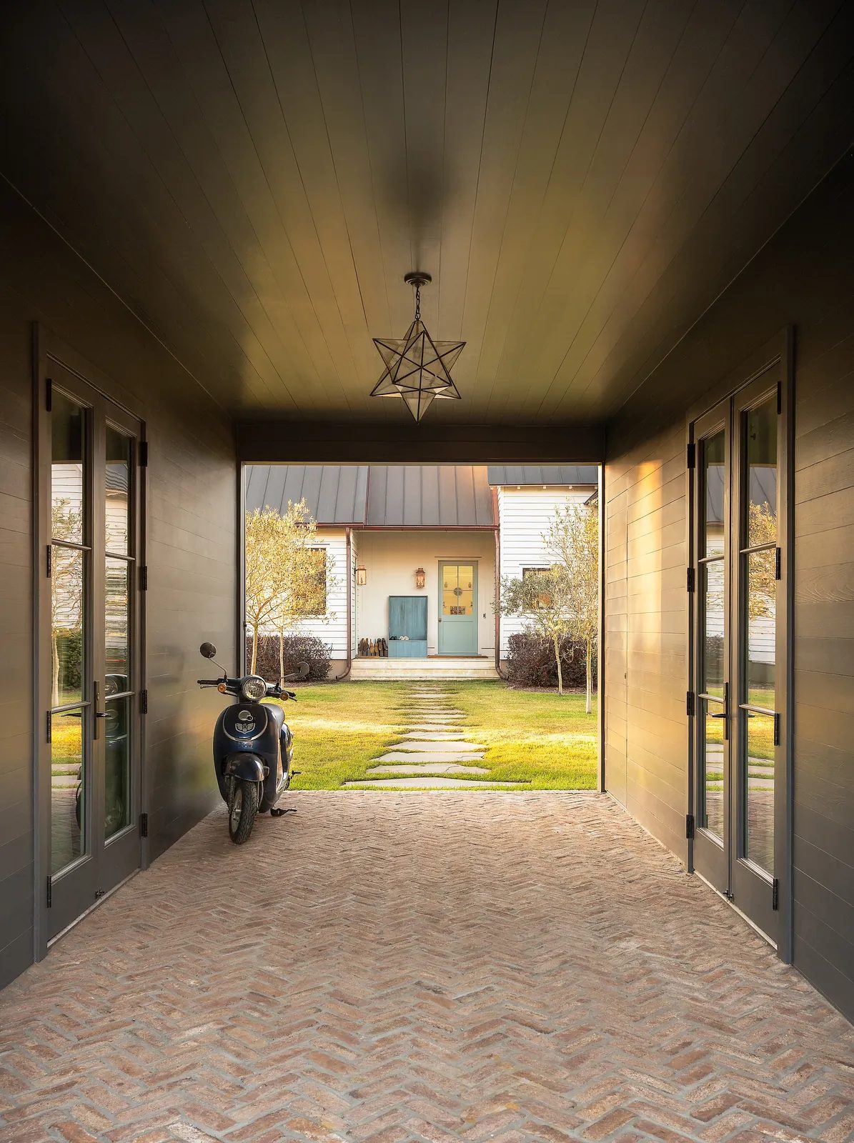Foyer with herringbone brick floor, glass doors, star pendant light, and view of a blue front door.