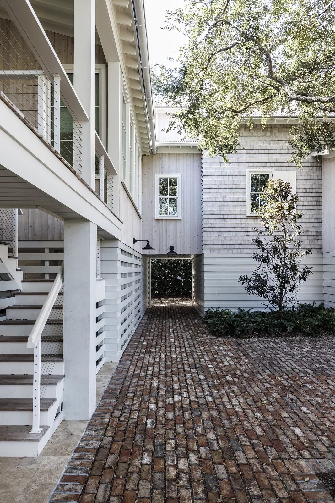 Exterior area with brick path, wooden siding structure, staircase, tree, and shrubs.