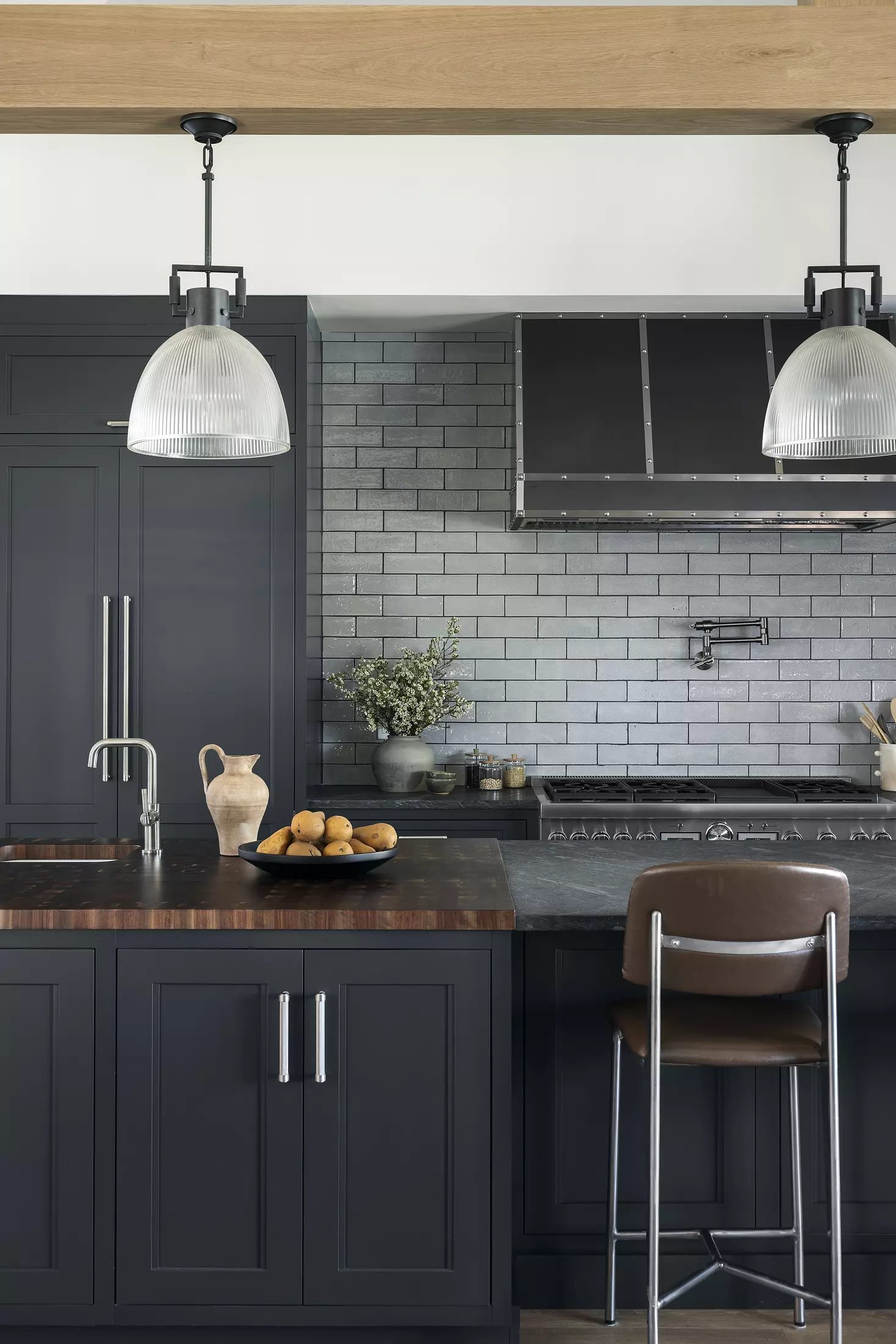 Kitchen with dark cabinetry, wood countertop, gray tile backsplash, fruit bowl, and bar stool.