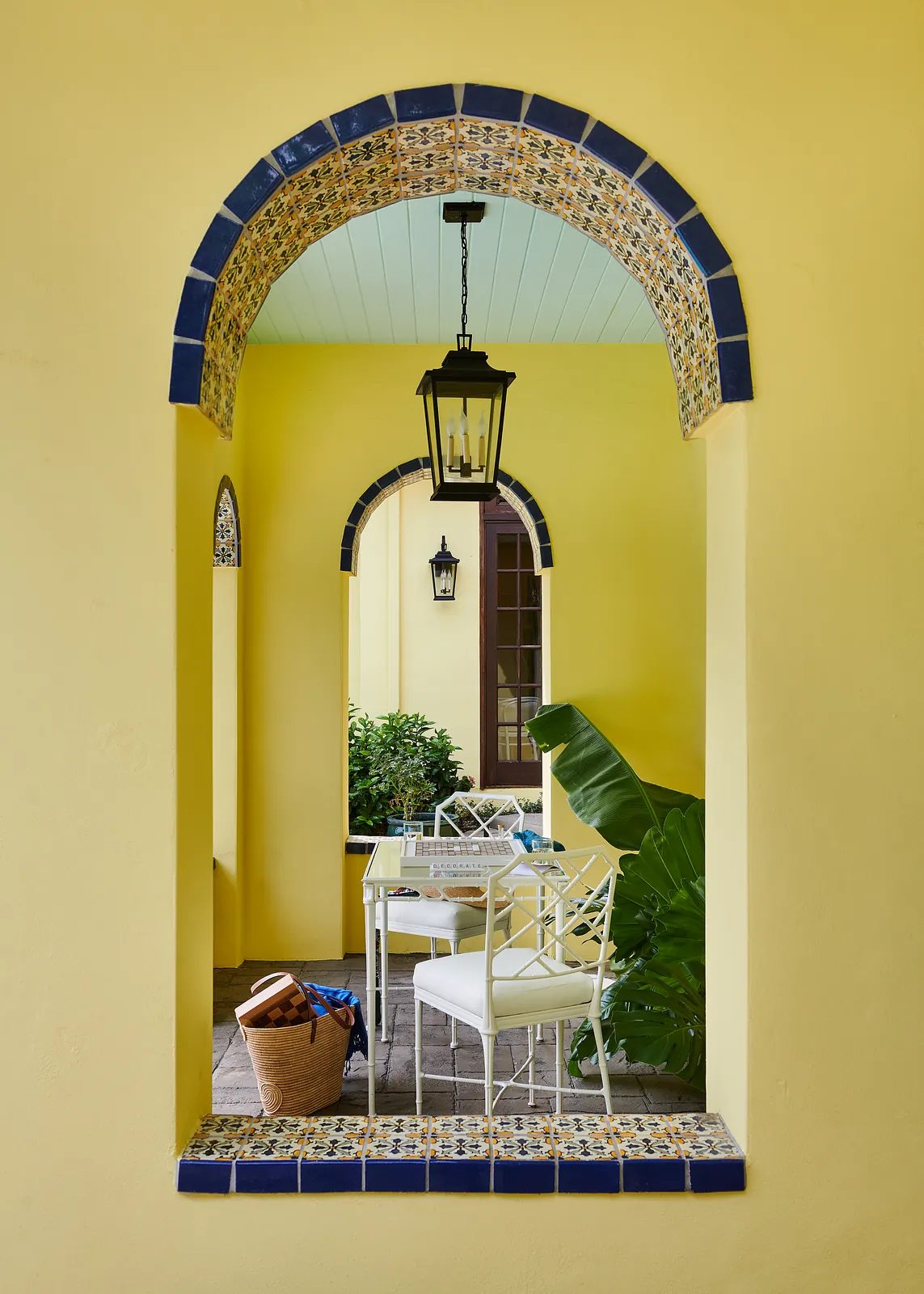 Patio with white table, chairs, woven basket, yellow walls, blue trim, and potted plants.