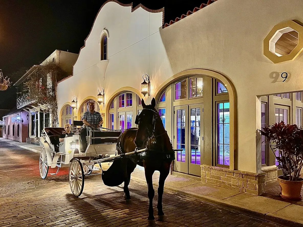 Exterior front view of a building with arched windows, horse-drawn carriage, and colorful lighting.