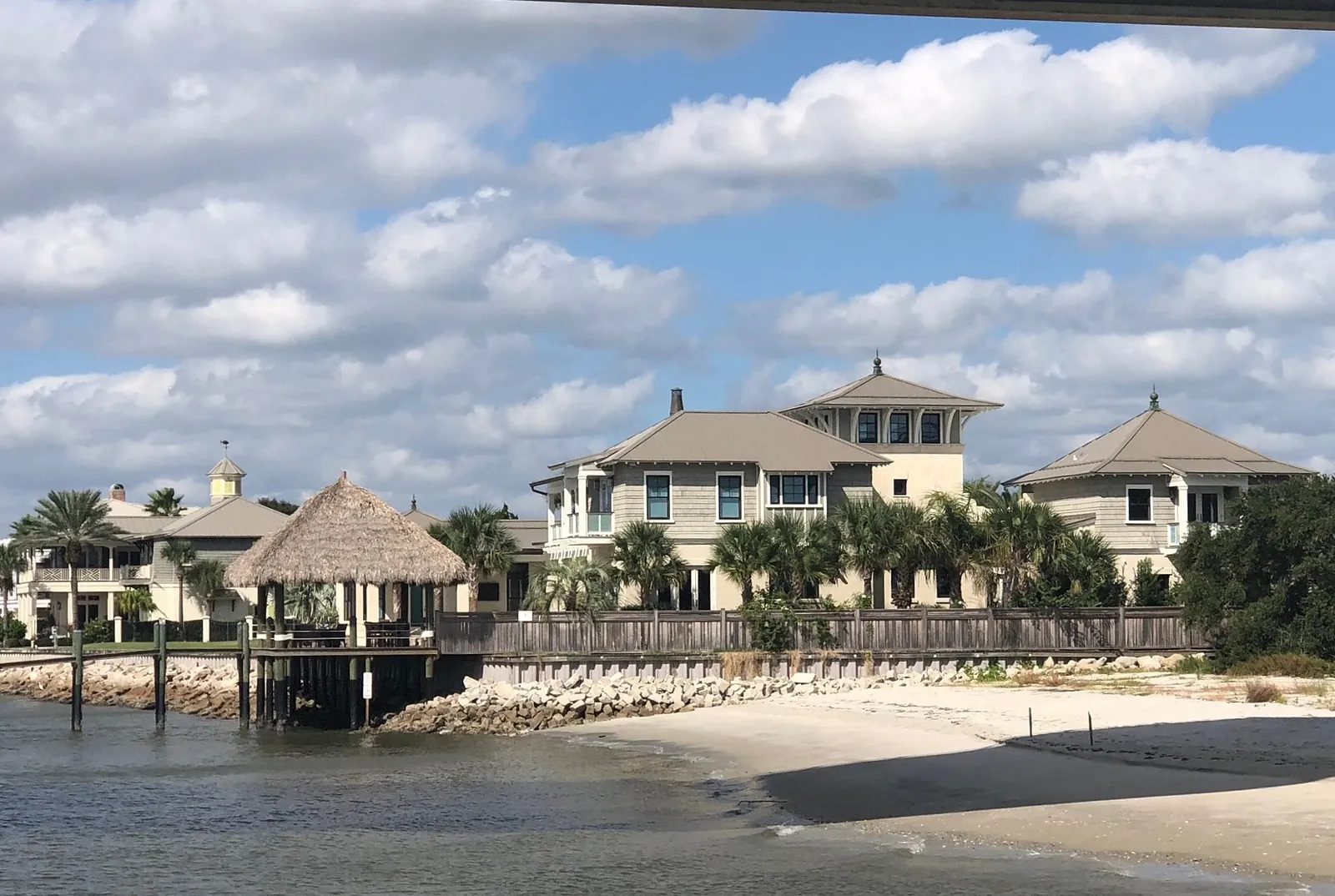 Coastal house exterior with multiple stories, balconies, gazebo, palm trees, and sandy beach.