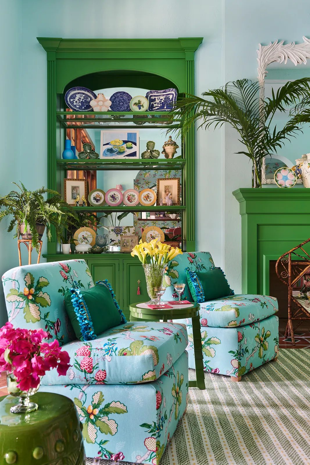 Living room with floral chairs, round table, green cabinet, plants, and blue walls.