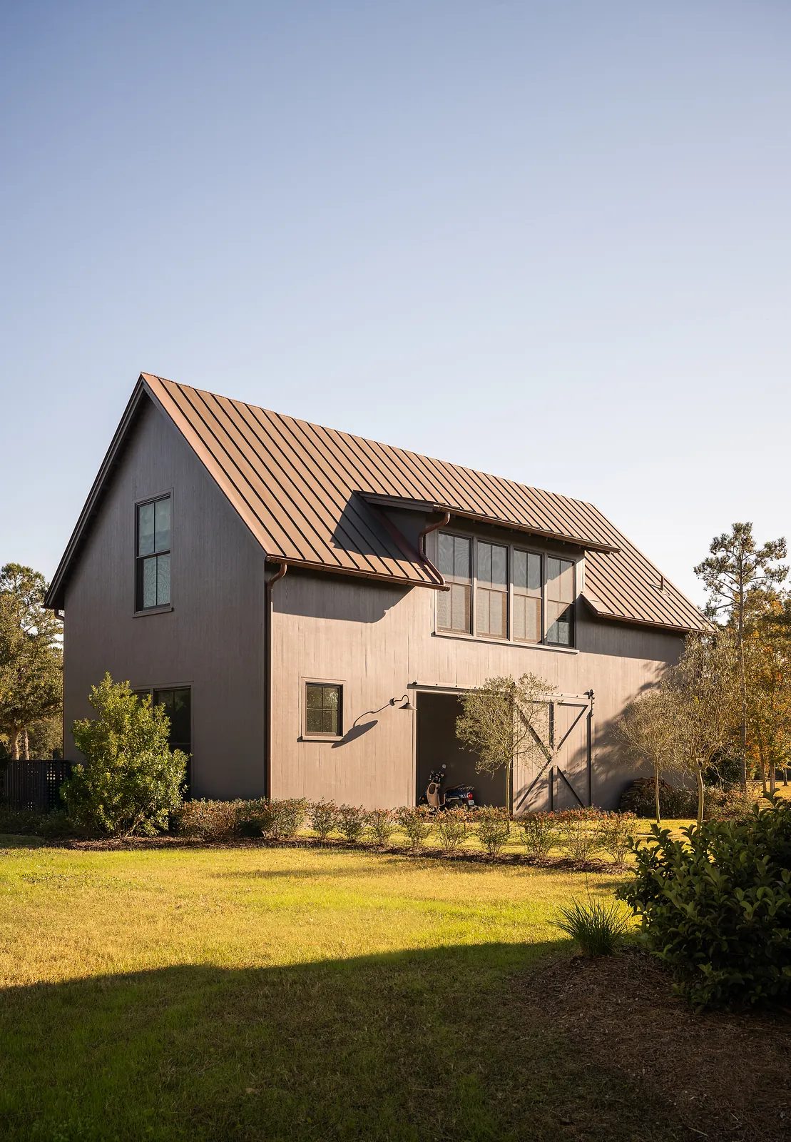 Exterior front view of a house with dark wood exterior, metal roof, large windows, and landscaped lawn
