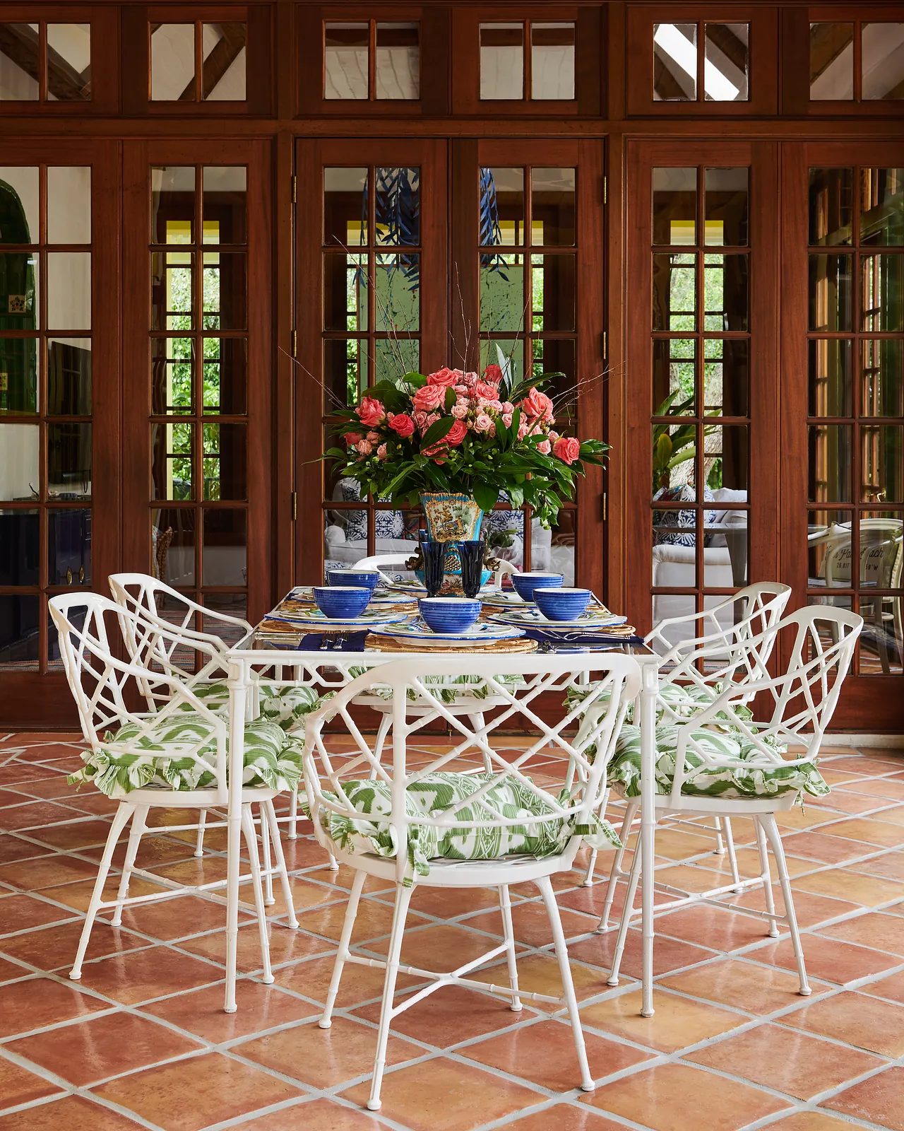 Dining room with white table, floral centerpieces, blue dishes, and white chairs with green cushions.