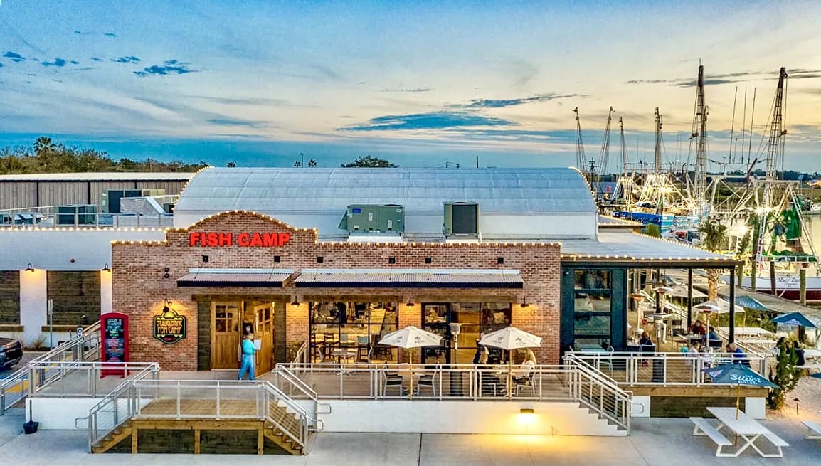 Exterior view of Fish Camp restaurant with brick facade, patio, large windows, and nearby sailboats.