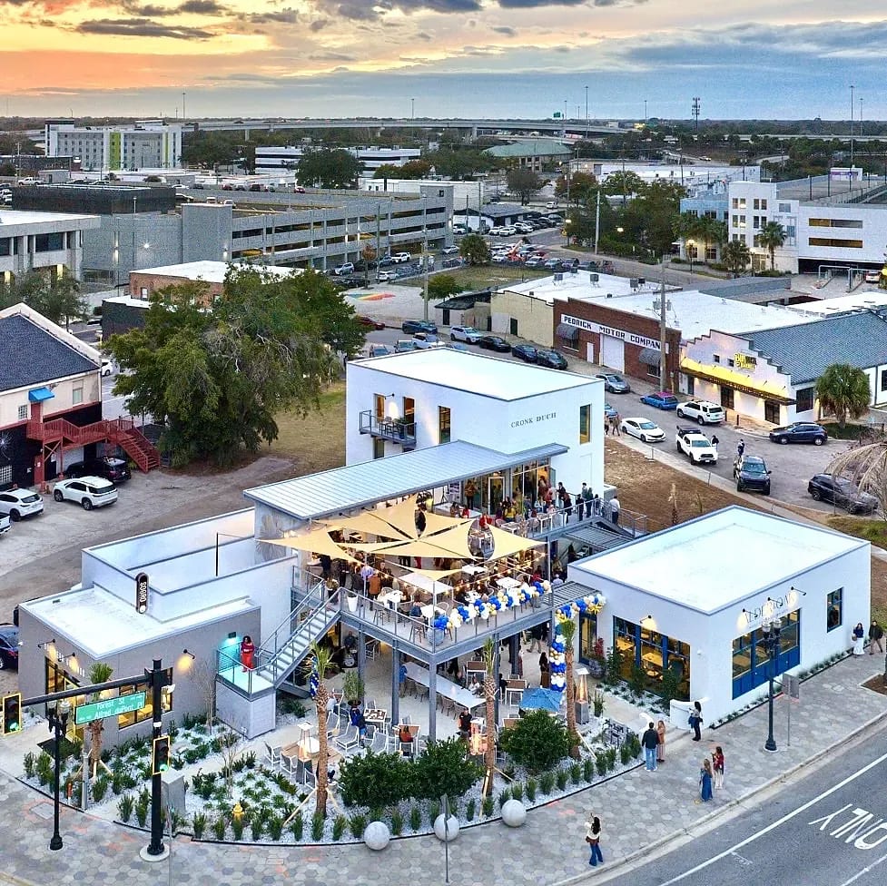 Outdoor commercial space with white buildings, terrace seating, and landscaping.