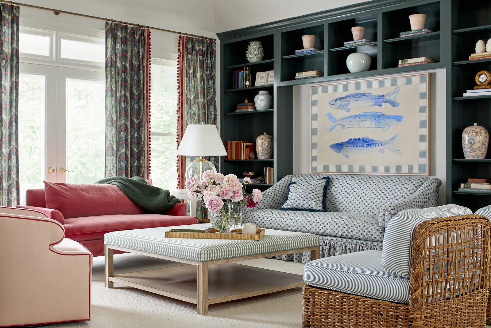 Living room featuring pink sofa, blue striped sofa, wooden coffee table, rattan chair, and dark shelving unit.