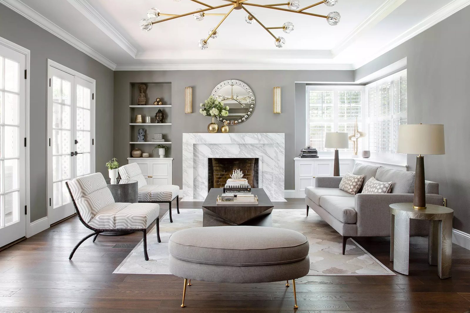Living room with gray sofa, patterned chairs, coffee table, area rug, marble fireplace, and natural light from windows.
