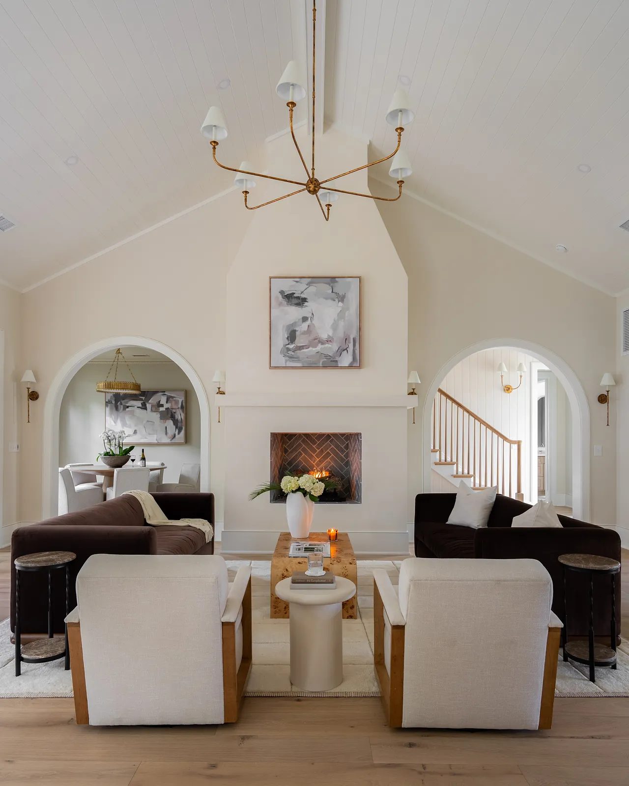 Living room with black sofas, white armchairs, round coffee table, fireplace, and vaulted ceiling with beams.