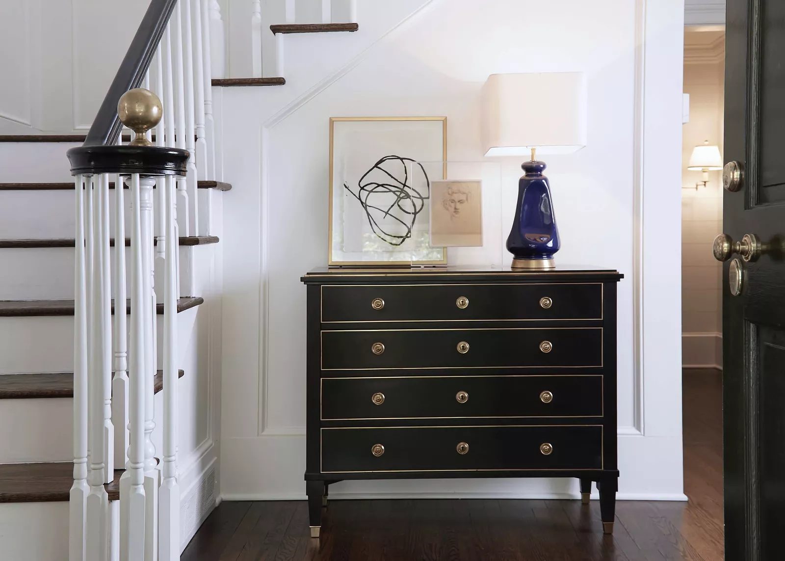 Foyer with black chest of drawers, abstract artwork, blue lamp, and wooden staircase with dark wood floor
