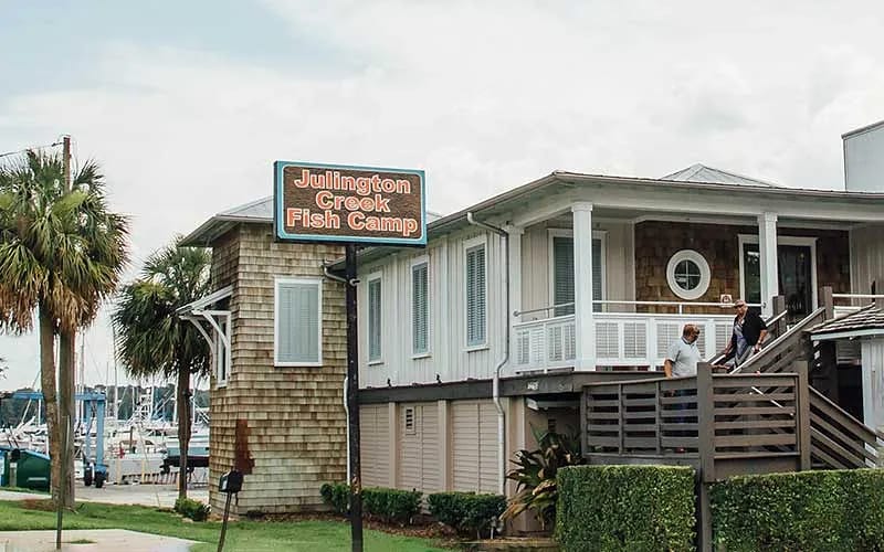 Exterior front view of Julington Creek Fish Camp with wooden siding, deck, and palm trees.