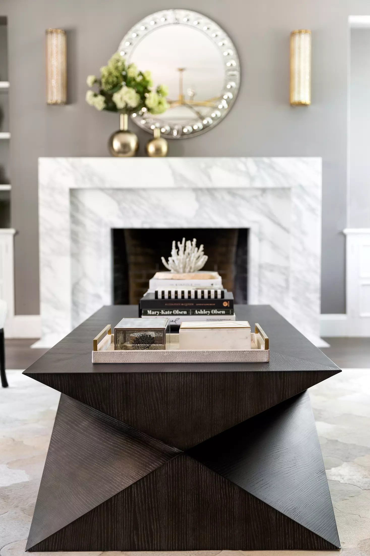 Living room with marble fireplace, geometric coffee table, decorative tray, and wall sconces