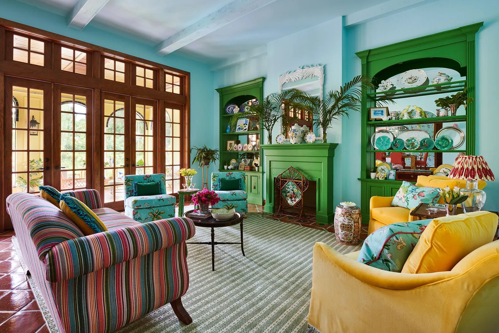 Living room with turquoise walls, striped sofa, yellow armchairs, and green built-in shelving unit.