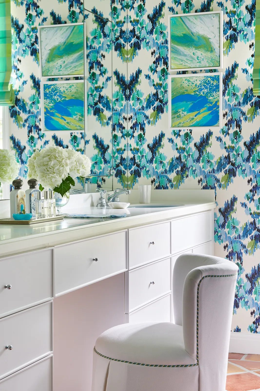 Bathroom with white vanity, blue-green wallpaper, and framed artworks.