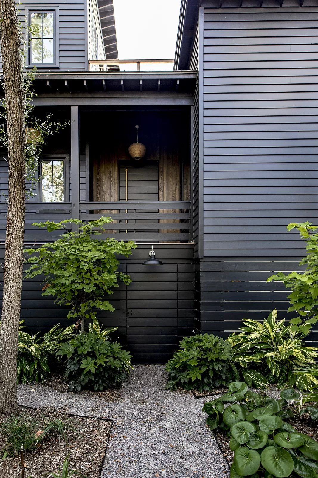 Exterior front with wooden door, gravel pathway, shrubs, and ceiling-mounted fixture above the entrance.