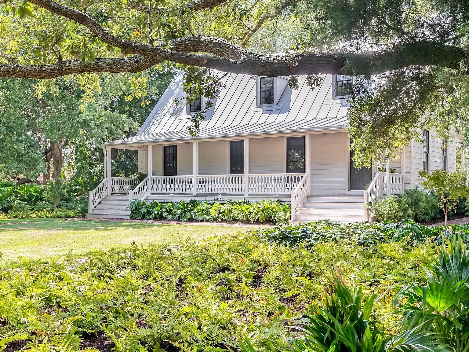 Front exterior view of house with metal roof, wooden siding, porch, and landscaped yard with ferns.