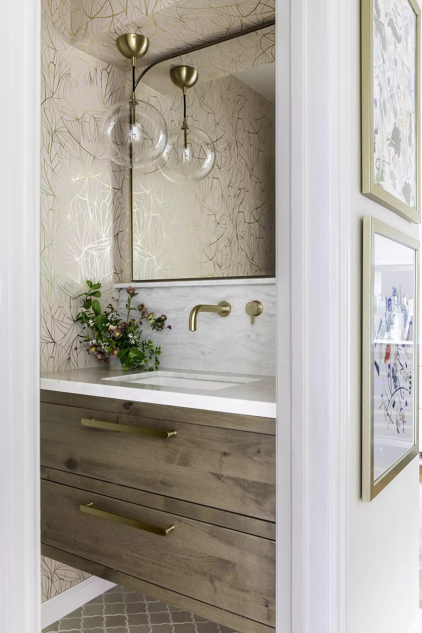 Powder room with wall-mounted sink, marble countertop, wooden cabinetry, floral wallpaper, and tiled flooring.