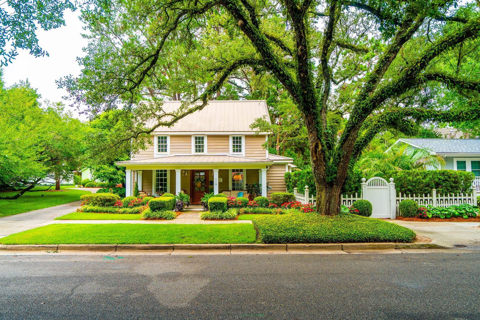 Front exterior of a two-story house with porch, landscaped yard, and large tree.