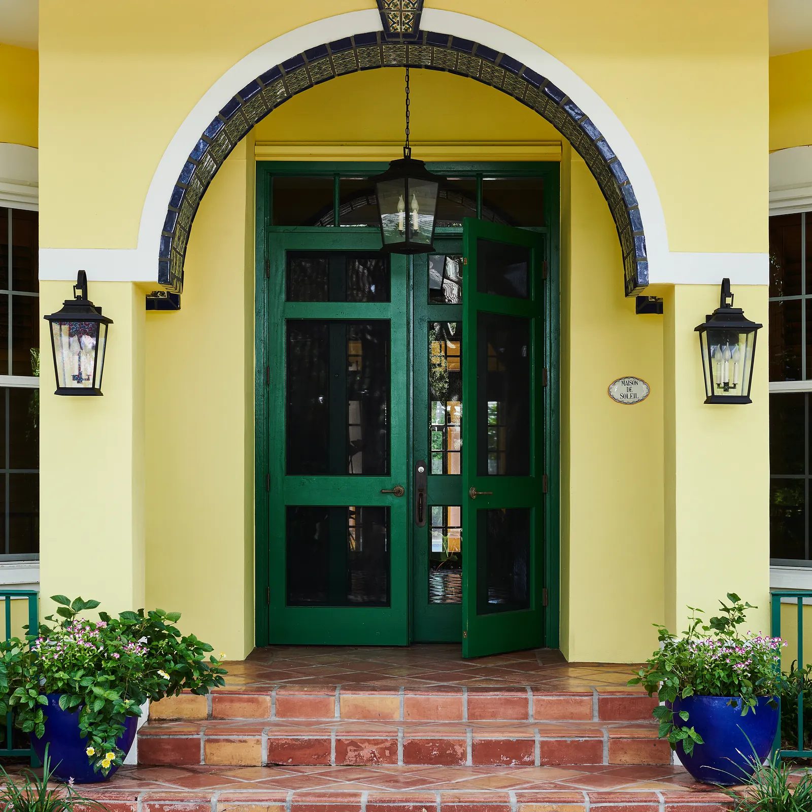 Exterior front entrance with double green doors, wall lamps, tiled steps, and planters with greenery.