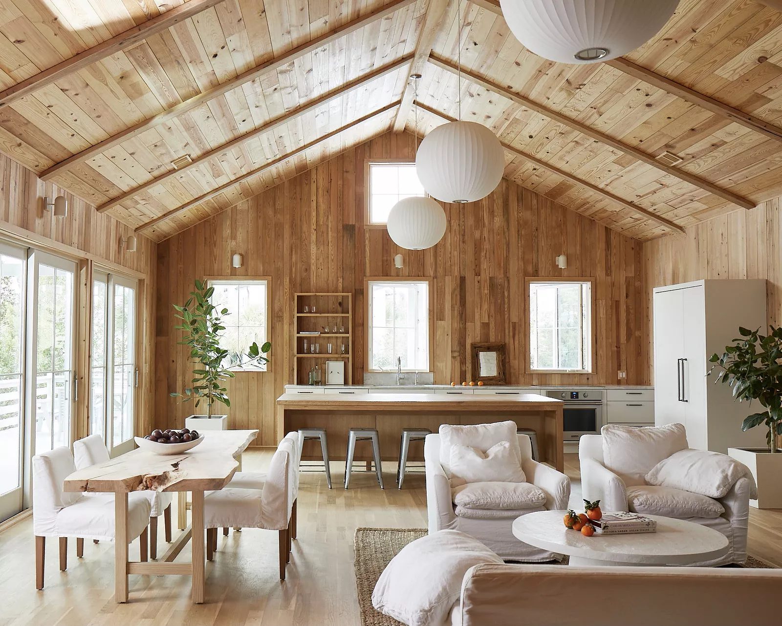 Living room with wood paneling, white sofa, dining table, and natural light from large windows and doors.