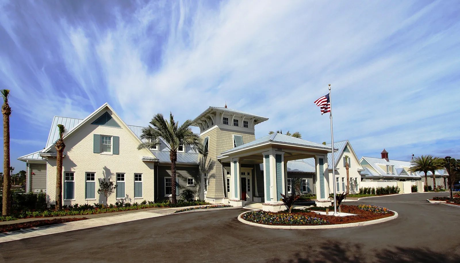 Exterior front view of a building with covered entrance, palm trees, and flower beds.