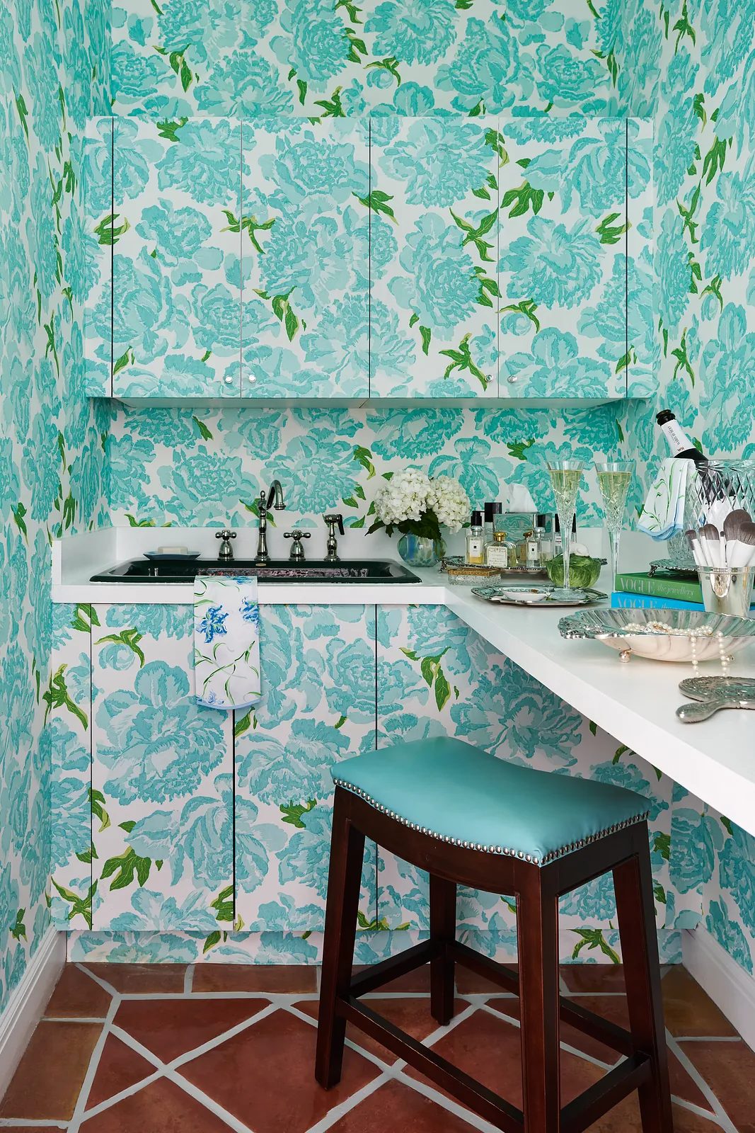 Powder room with floral wallpaper, white countertop, wood stool, and geometric tiled floor.