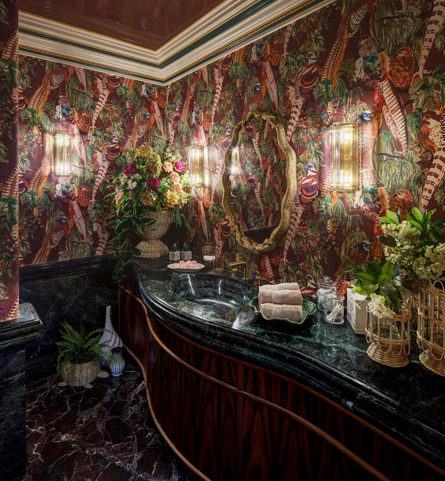 Powder room with curved marble vanity, floral wallpaper, sconces, and decorative decor elements.