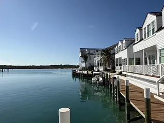 Exterior front view with dock, boats, white buildings, palm trees, and calm water.