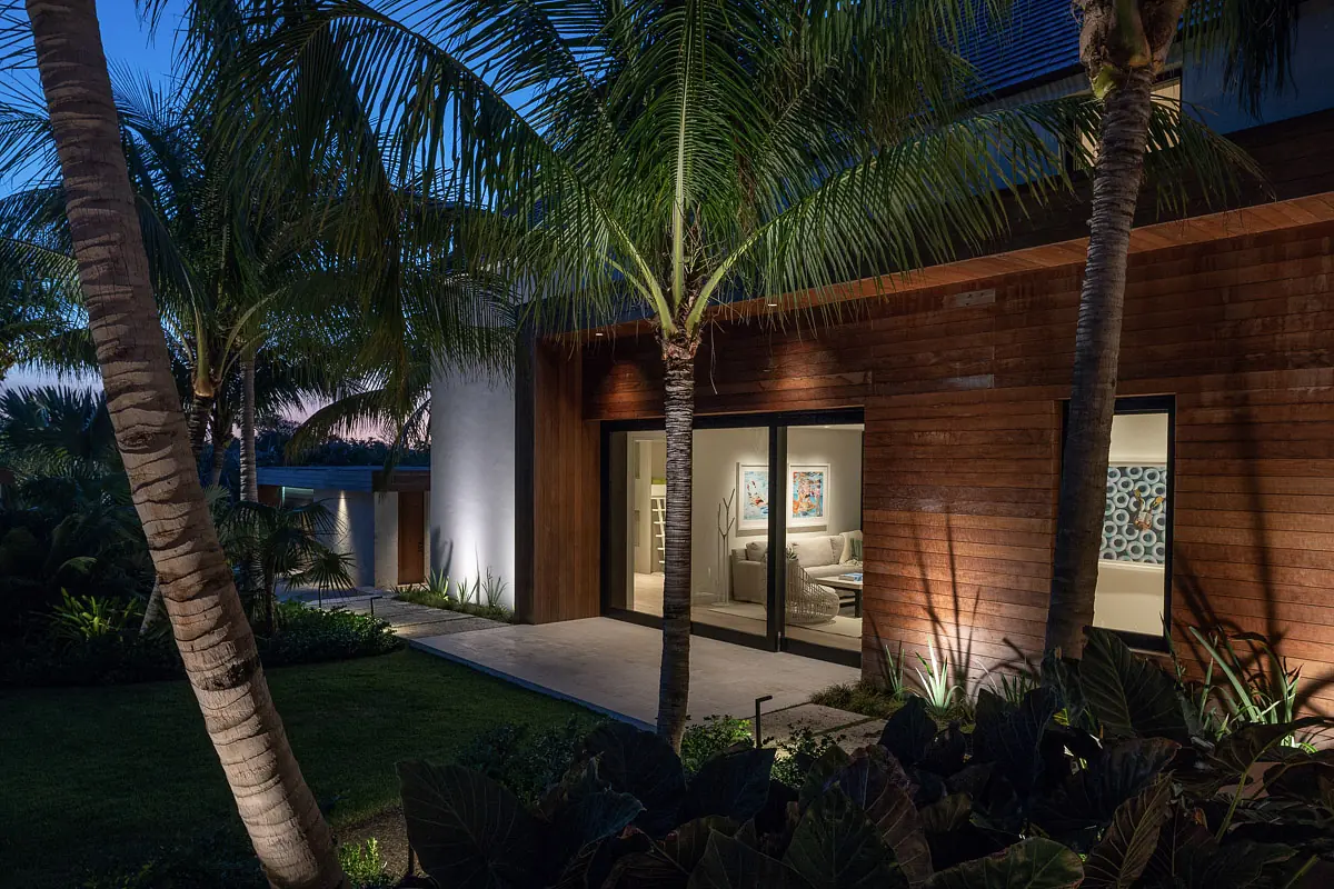 Outdoor rear view with modern home, large glass doors, wooden siding, palm trees, and landscaped garden.