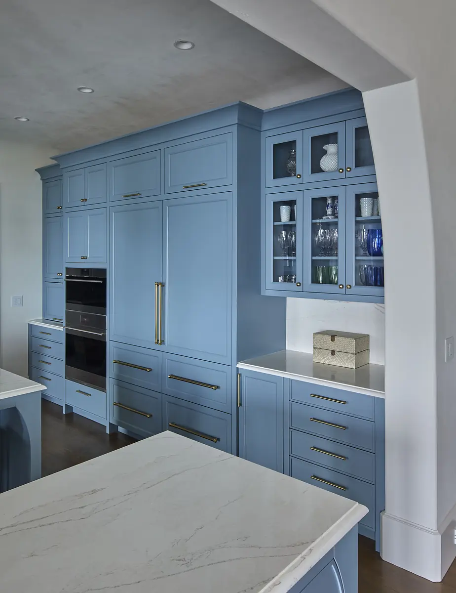 Kitchen with blue cabinetry, marble countertop, and glass-front cabinetry displaying dishware