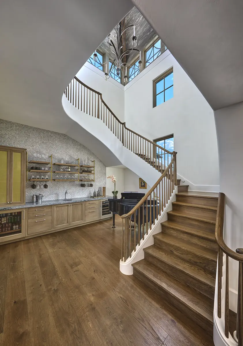 Foyer with curved staircase, small bar, hardwood floor, large windows, and vaulted ceiling.