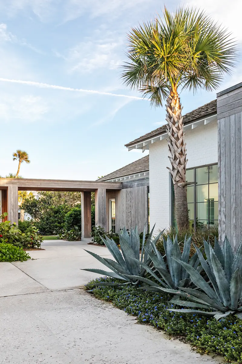 Exterior front view of house with driveway, tropical landscaping, and wooden accents.