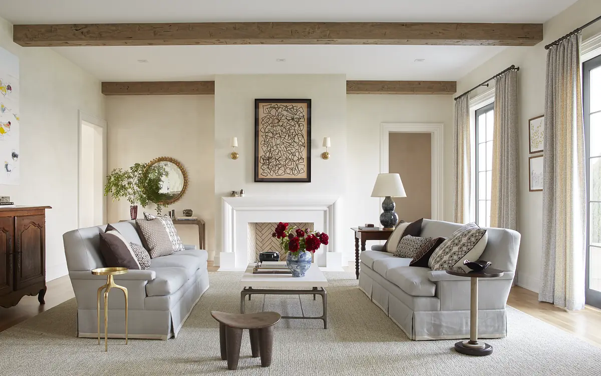 Living room with gray sofas, coffee table, area rug, fireplace, mirror, and windows with gray curtains.