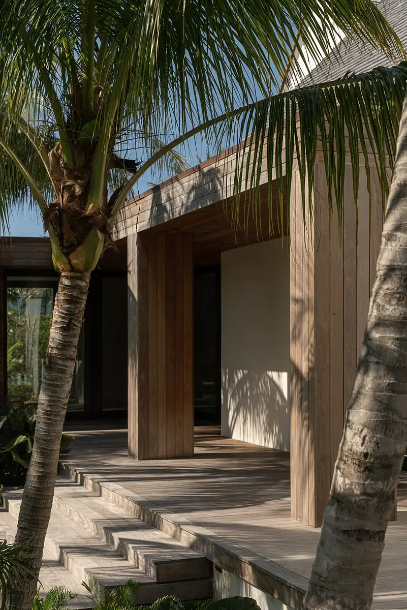 Exterior front with wooden deck, large glass doors, and surrounding palm trees.