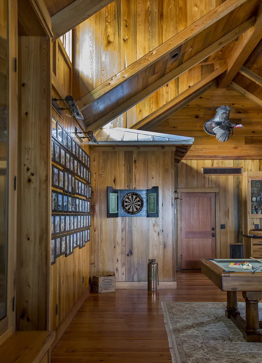 Room with wood-paneled walls, dartboard, pool table, slanted ceiling, and wooden floor.