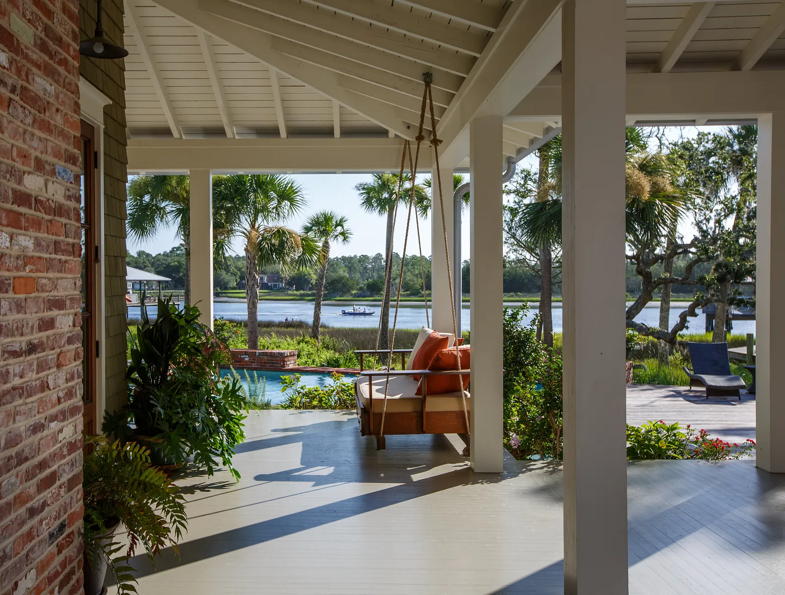 Patio with swing chair, orange cushions, potted plants, and views of a water body and palm trees