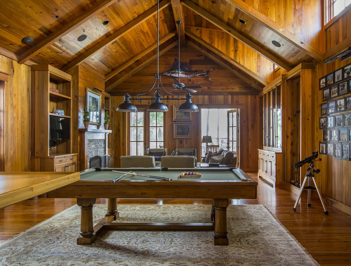 Living room with wooden walls, pool table, sofa, area rug, photographs, telescope, and fireplace with natural light.