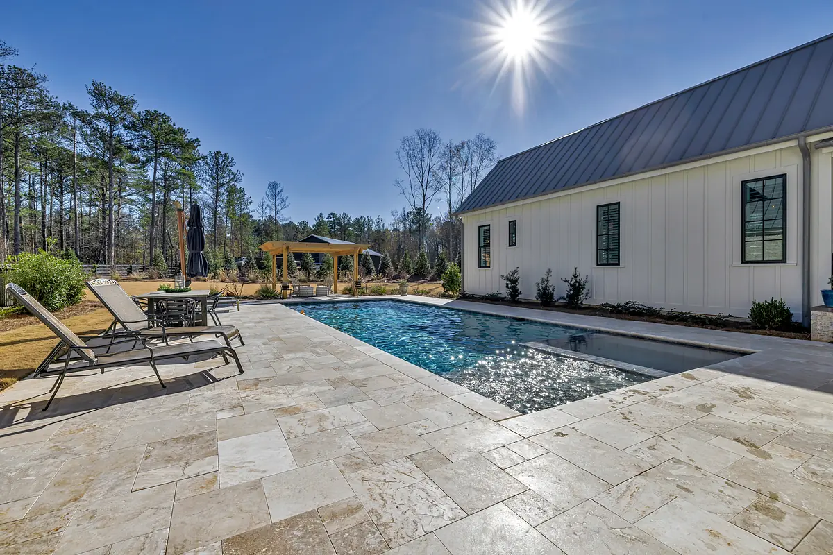 Patio with swimming pool, stone tiles, lounge chairs, and shaded gazebo surrounded by grass and trees.