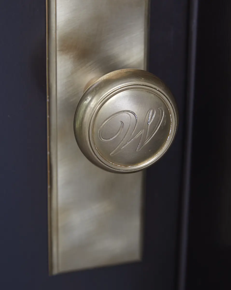 Close-up of a brass door knob with an engraved 'W' on a dark door.