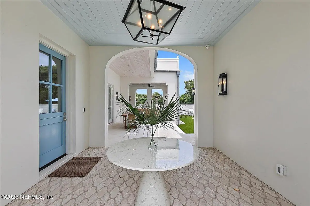 Foyer with round marble table, potted plant, welcome mat, and arched entrance with blue door.