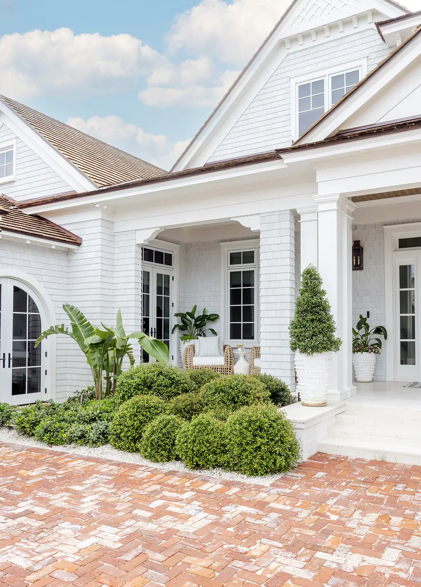 Exterior front of house with white facade, large doors, windows, porch, plants, and brick pathway