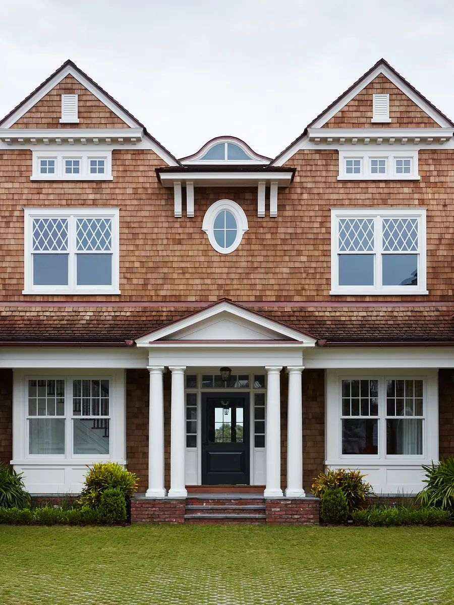 Front exterior of a house with wooden shingles, columns, gabled roof, and large windows.