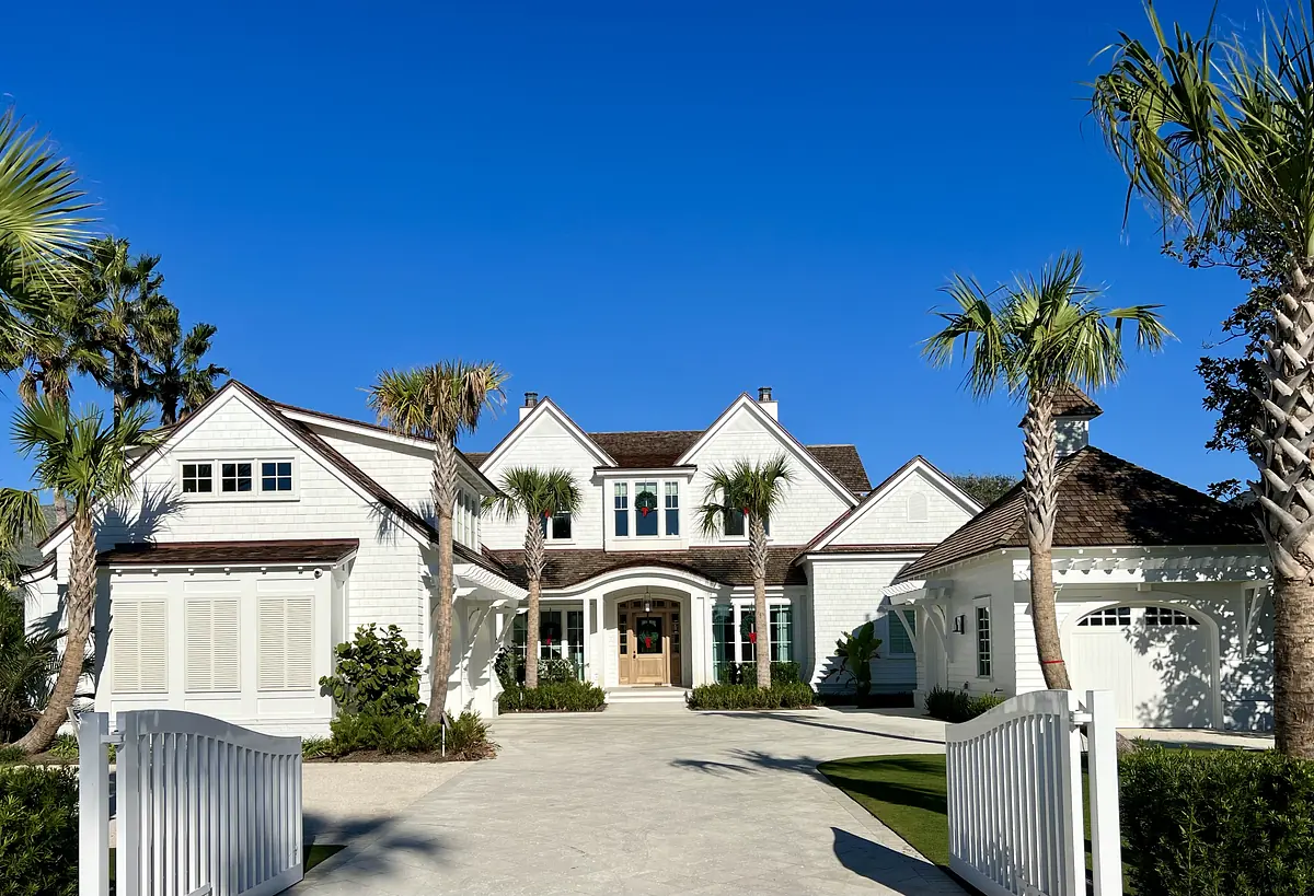 Front exterior of a house with white siding, brown shingle roof, palm trees, and arched entryway.