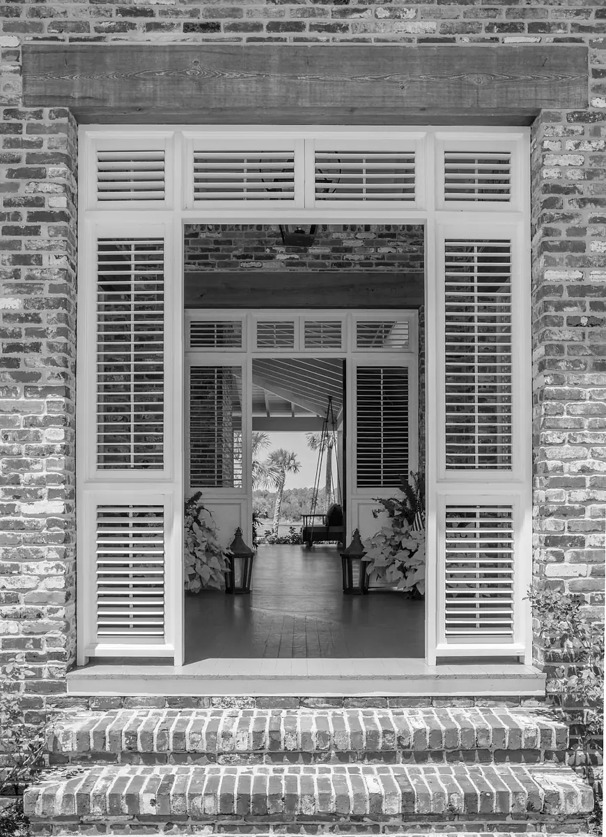 Exterior front view with brick facade, double doors, white shutters, steps, lanterns, and potted plants.