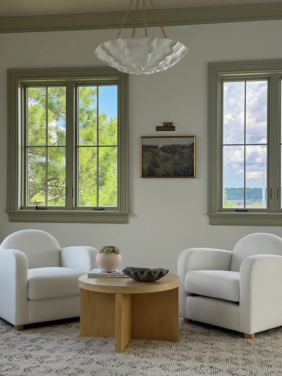 Living room with white armchairs, round wooden coffee table, area rug, and large windows with scenic view.