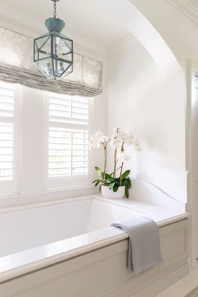 Bathroom with white freestanding tub, marble surround, potted orchid, and ceiling lantern.
