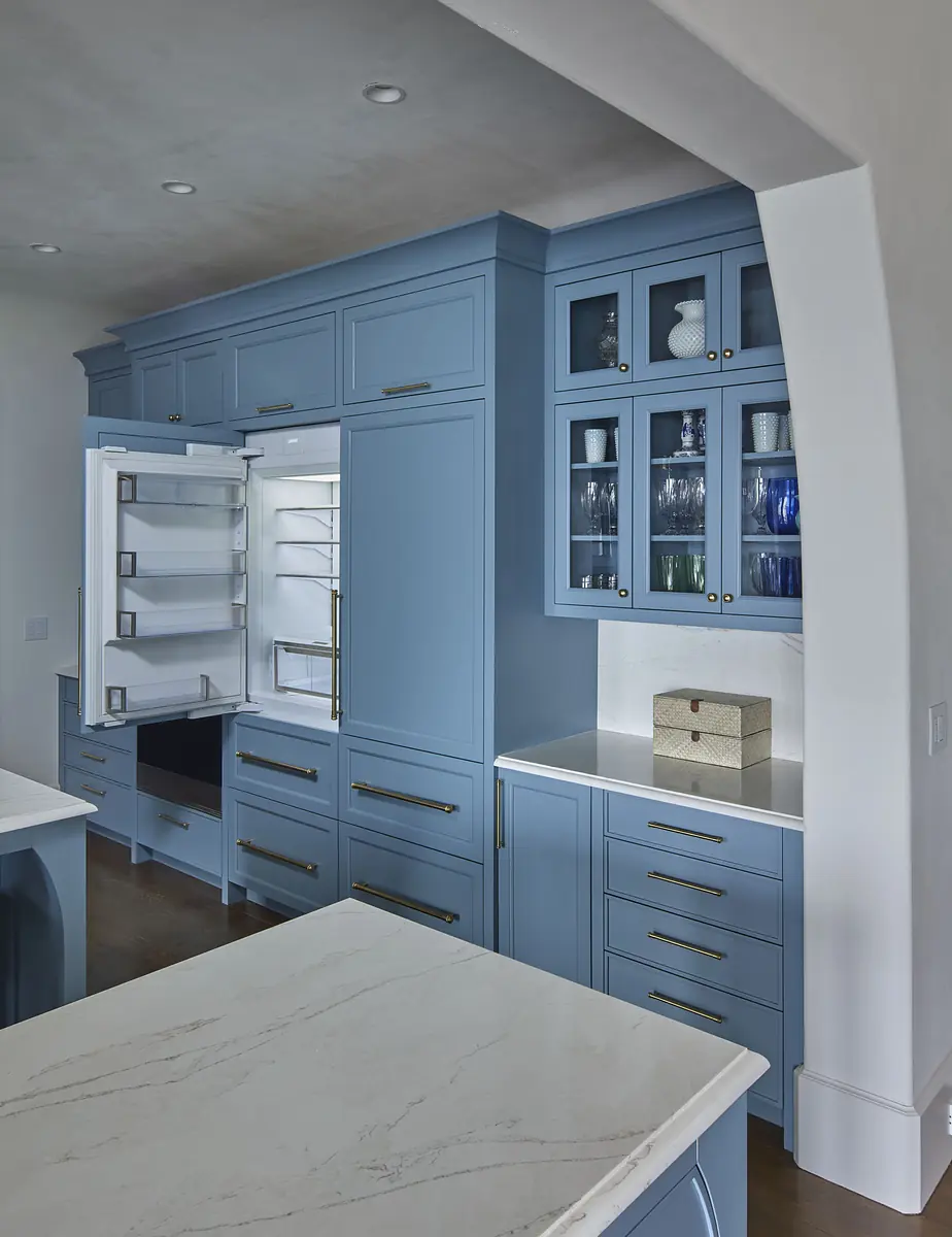 Kitchen with blue cabinetry, white marble countertop, island, and glass-front cabinets for displaying glassware.