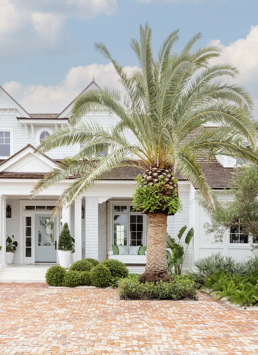 Front exterior with brick pathway, palm tree, columns, double doors, and surrounding plants.