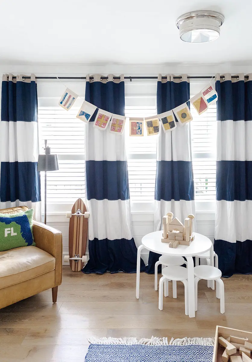 Living room with striped curtains, tan sofa, white table, wooden toys, and a decorative banner